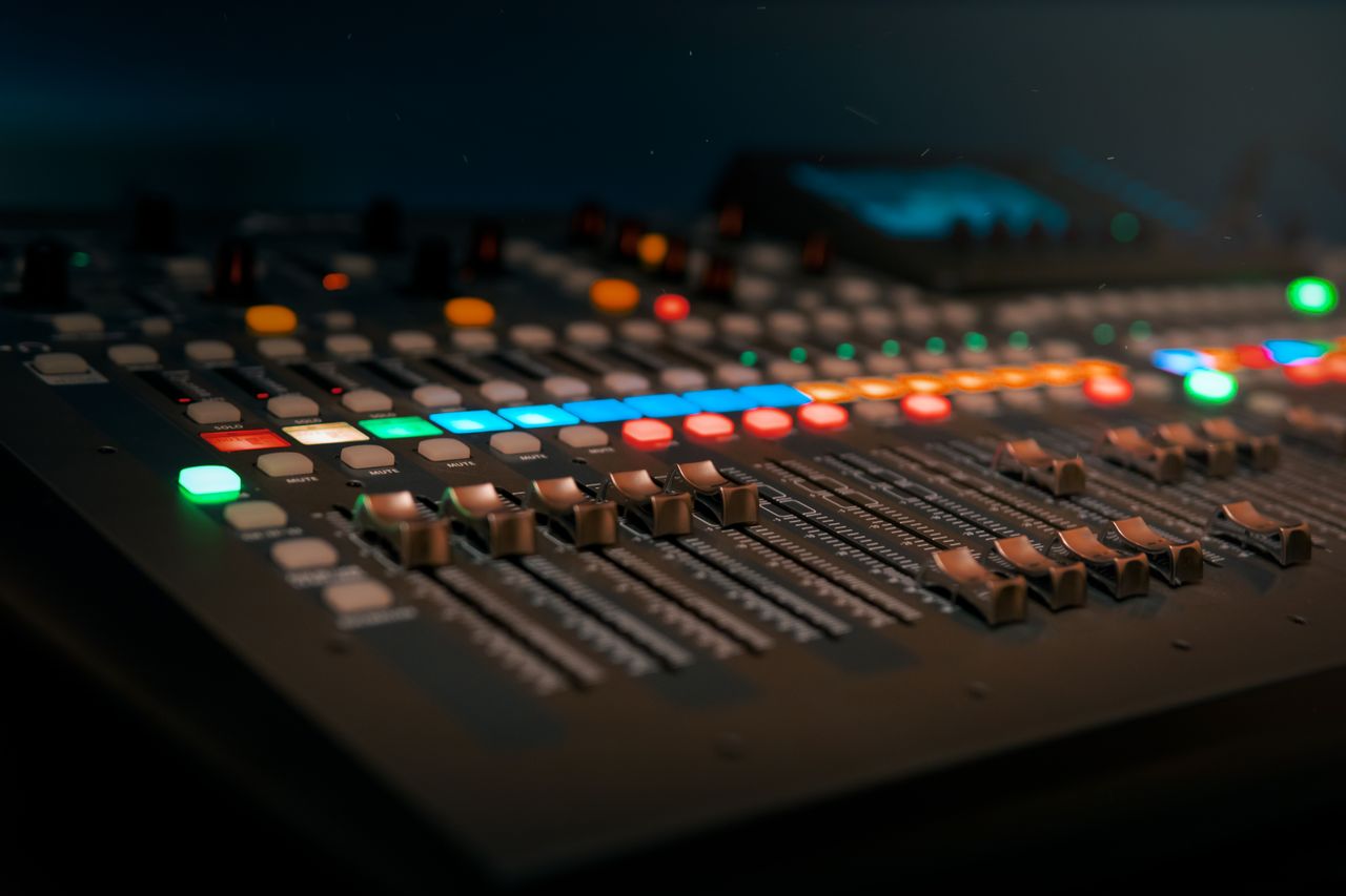 Services Close-up of a professional sound mixer with colorful glowing controls in a dimly lit studio.